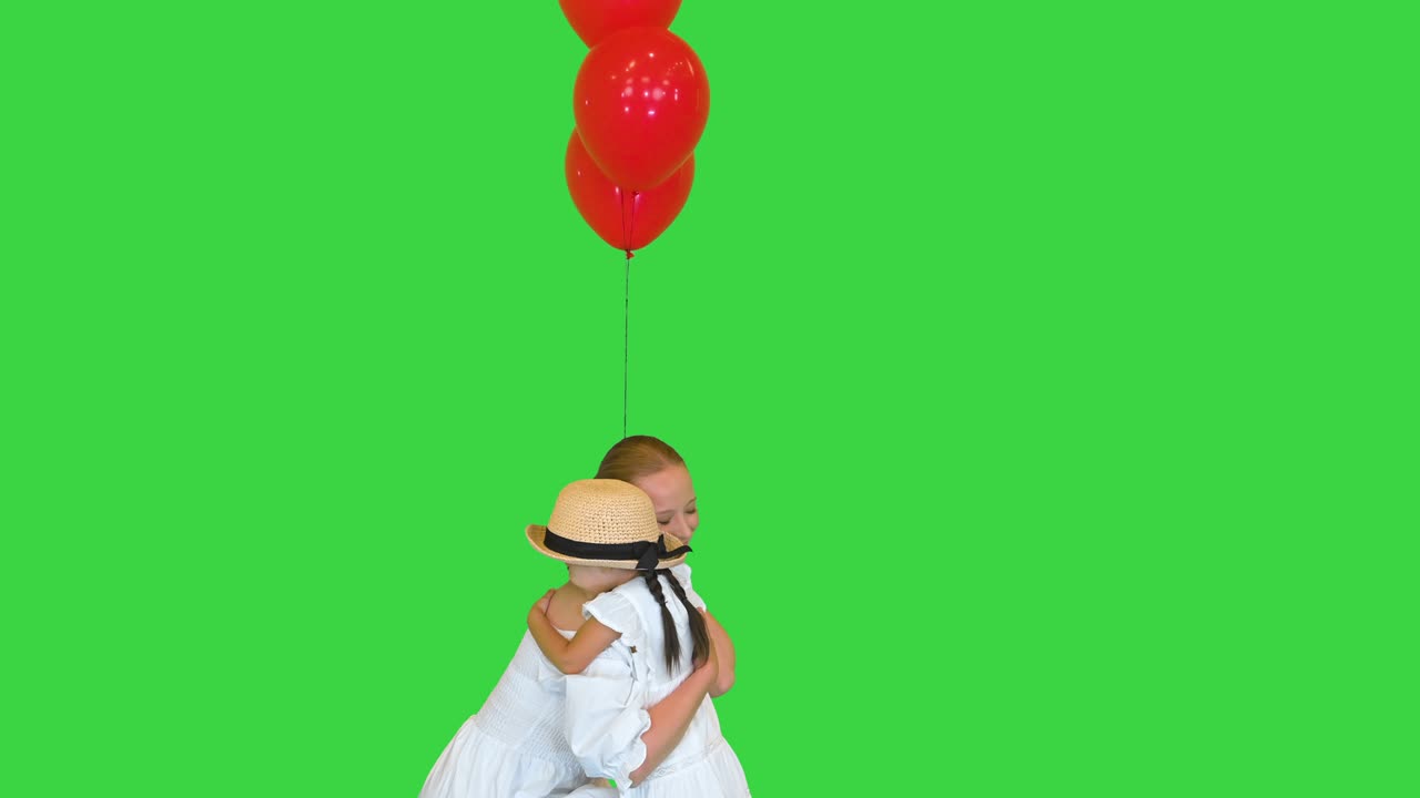 미소 짓는 어머니와 딸은 녹색 스크린, 크로마 키에 빨간 풍선을 들고 안고 있습니다.