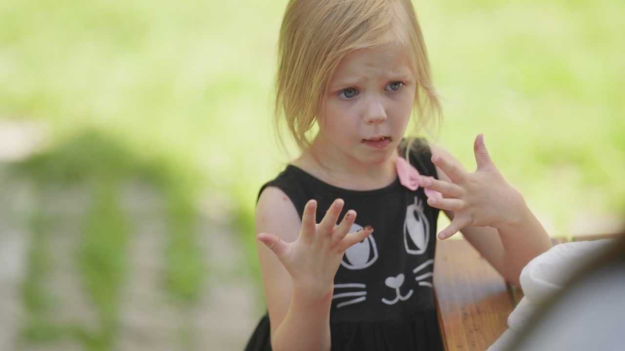 그녀의 얼굴에 슬프고 실망한 표정을 가진 작은 금발 소녀는 그녀의 더러운 손을보고
