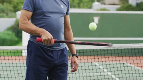 Video-De-La-Sección-Media-De-Un-Hombre-Mayor-Birracial-Sosteniendo-Una-Raqueta-Y-Lanzando-Una-Pelota-En-Una-Cancha-De-Tenis.