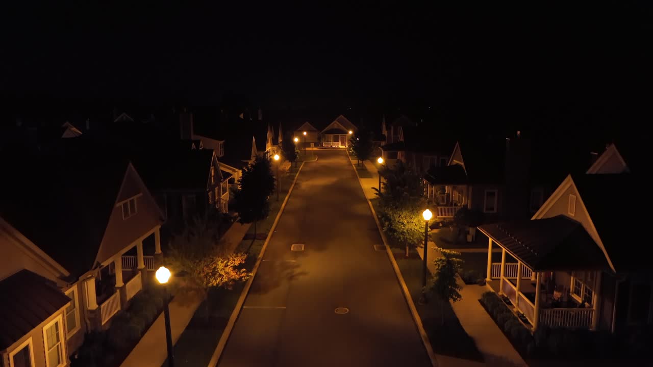 Empty road with lighting lantern in quiet american neighborhood at night. Aerial rising wide shot. Large luxury upscale houses and homes in suburb of United States.