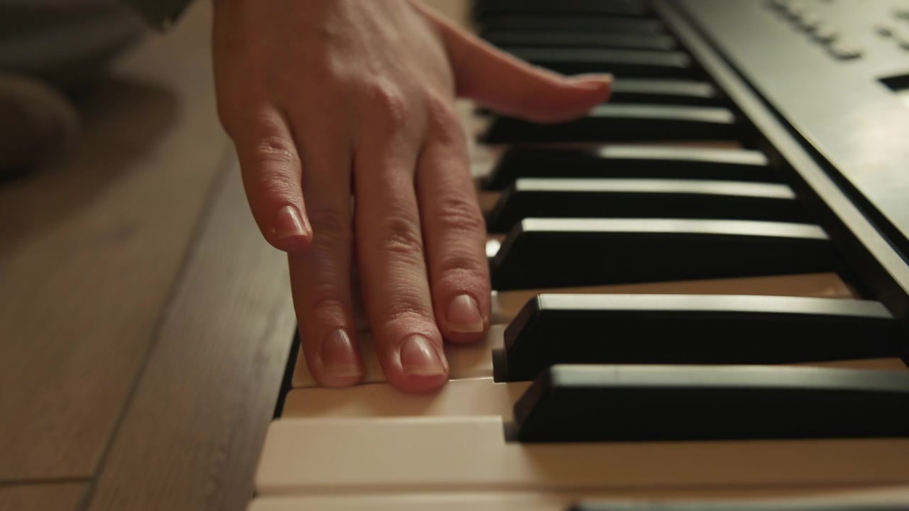 Low-angle close-up of adult hands actively playing keyboard in warm home studio, fingers sliding, pressing, and changing position across black and white keys with fluid musical movement