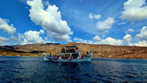 tour boat full of people sailing on the sea with mountains under a blue sky