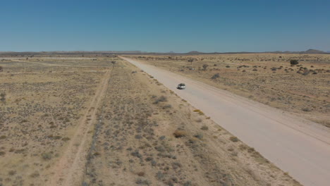 Toma-Aérea-Giratoria-De-Seguimiento-De-Un-Vehículo-En-Movimiento-Rápido-En-Una-Carretera-Vacía-Y-Polvorienta-En-El-Desierto