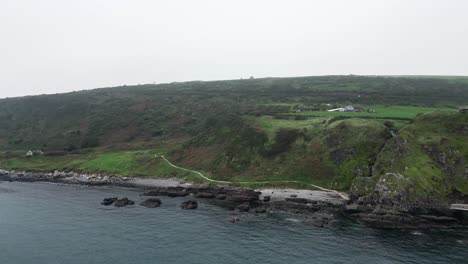 Aerial-dolly-forward-shot-of-the-Gobbins-Cliffs-in-Northern-Ireland-during-an-adventurous-journey-overlooking-the-coast-road,-calm-sea-and-rocks-on-a-cloudy-morning-on-an-expedition