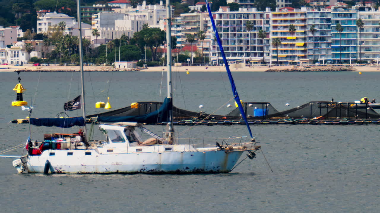 Juan-les-Pins, France - April 3, 2025: Rusty, white boat docked on the sea with the buildings and the mountains on the background