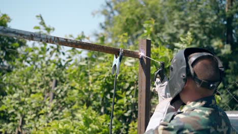 craftsman in mask welds upper detail to fence pole in garden