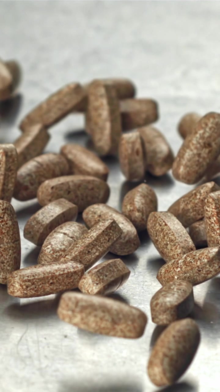 Brown Speckled Pills Falling onto a Metallic Surface in Slow Motion