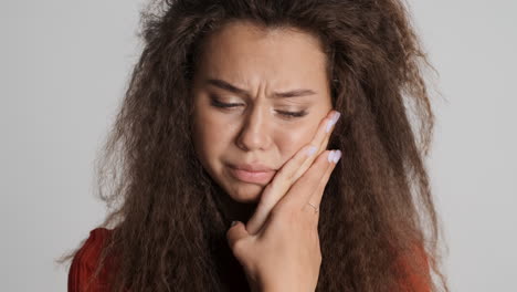 mujer caucásica de cabello rizado con dolor de dientes frente a la cámara.