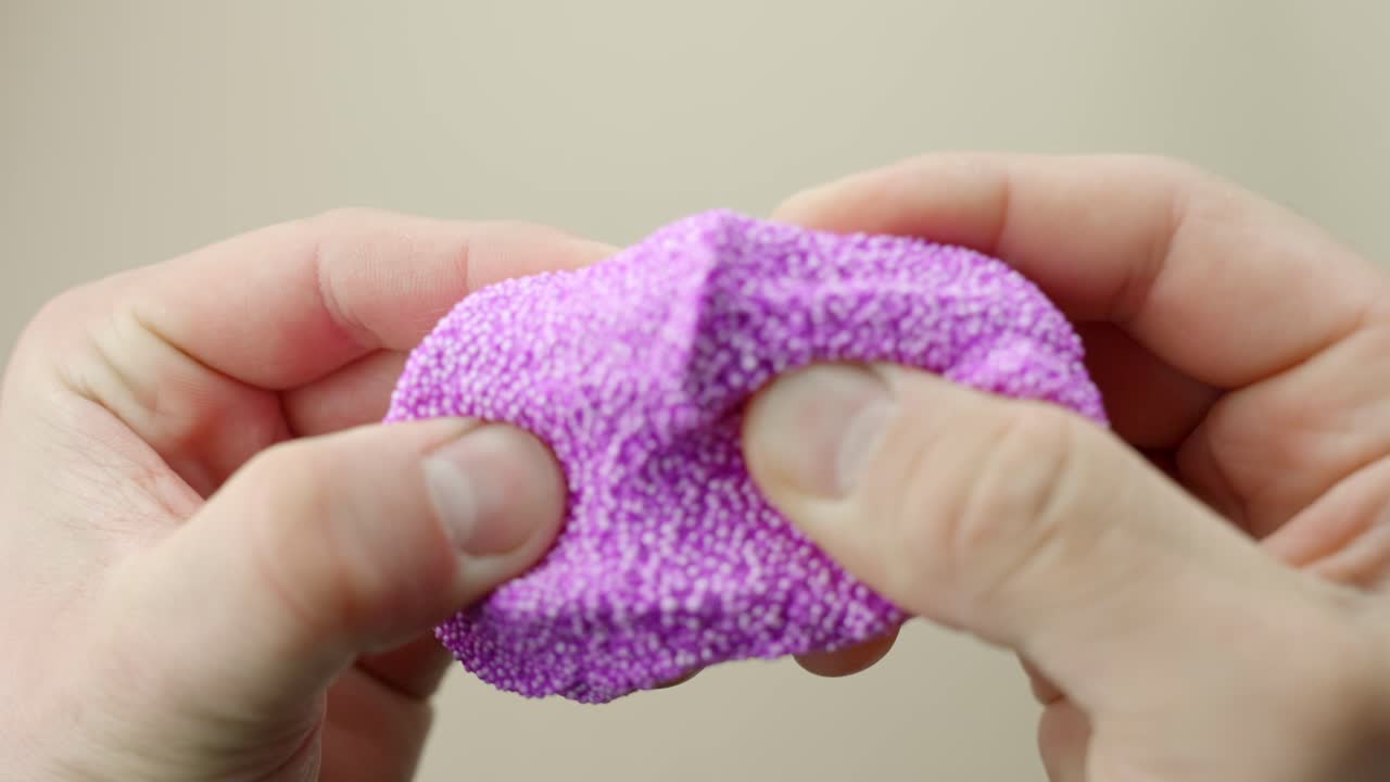 Close-up of fingers squishing purple foam slime in first person view, slow motion