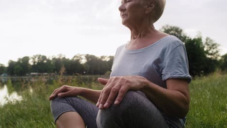 Mujer-Mayor-Tranquila-Meditando-En-El-Parque-Junto-Al-Lago