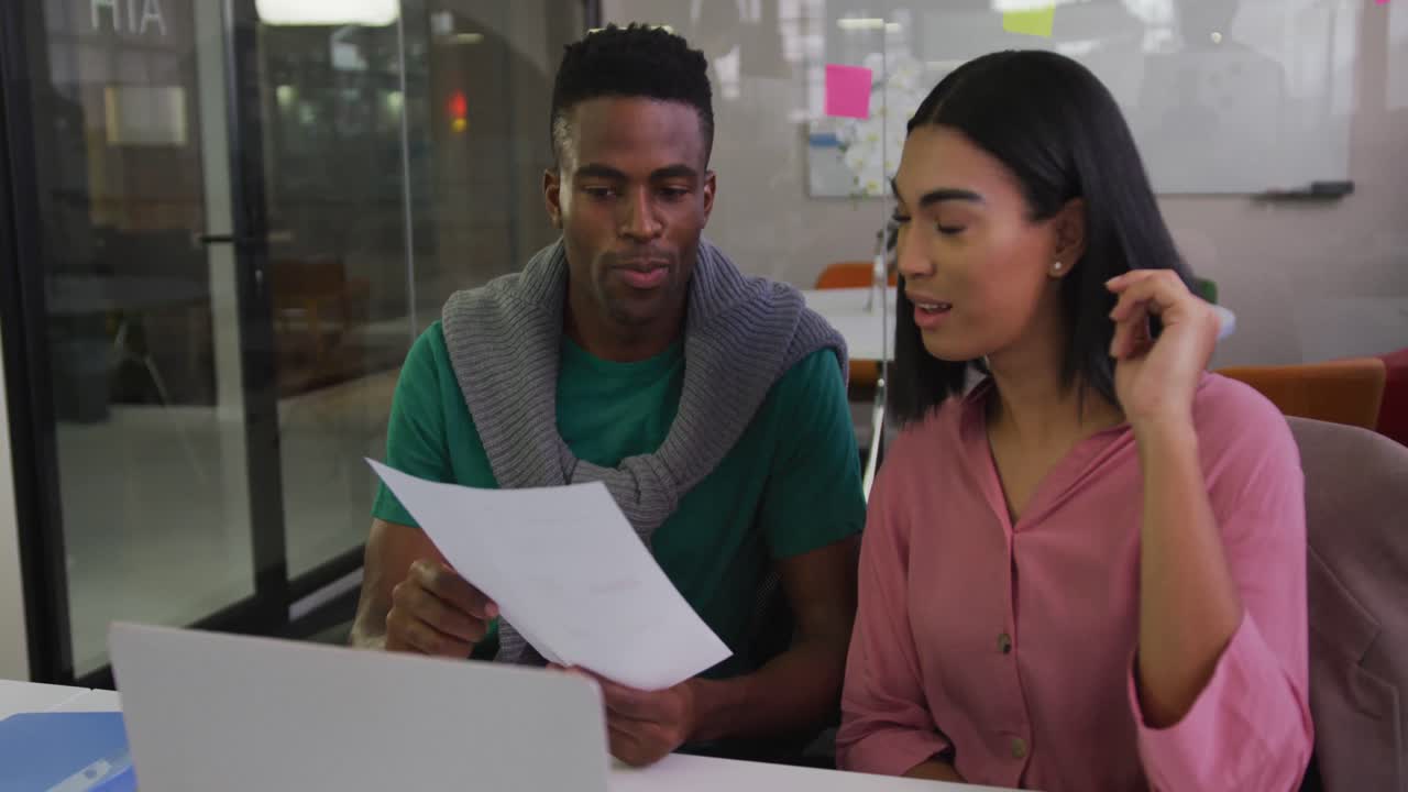 Diverse male and female business colleagues sitting at desk analyzing document and smiling