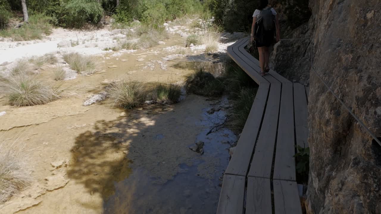 Hiker walking on wooden trail at Parrizal de Beceite in sunny Spain wilderness