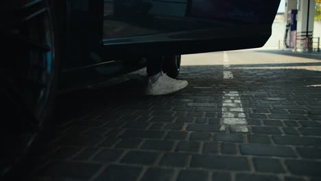 close-up shot of a guy in white sneakers getting out of a dark gray convertible and going to fill up his car at a gas station