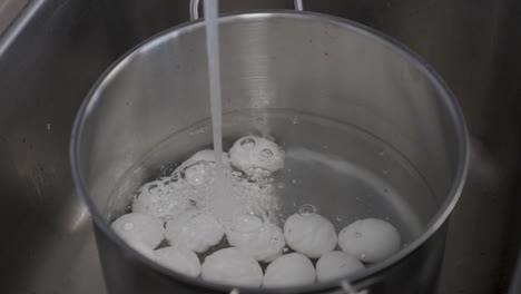 water filling up a cooking pot filled with eggs ready to boil