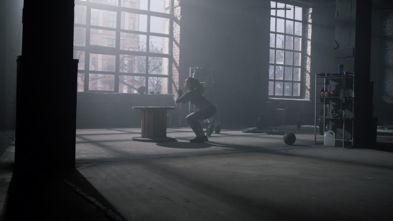 Donna che salta su una cassa di legno in palestra. Ragazza che esegue squat profondi con salti.