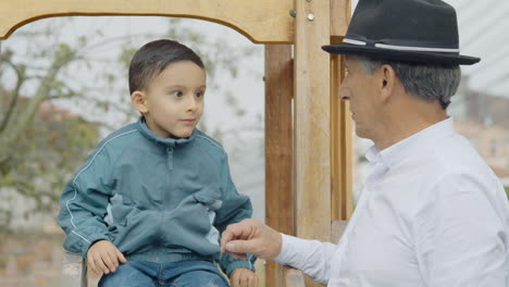 a tender moment between grandfather and grandson as they play together in a wooden playhouse with a slide in the backyard.
