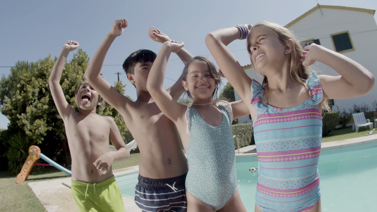 Children dancing at poolside raising hands, having fun together.