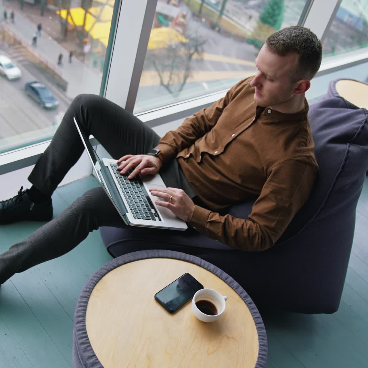 man working with laptop while sitting on armchair near panoramic window