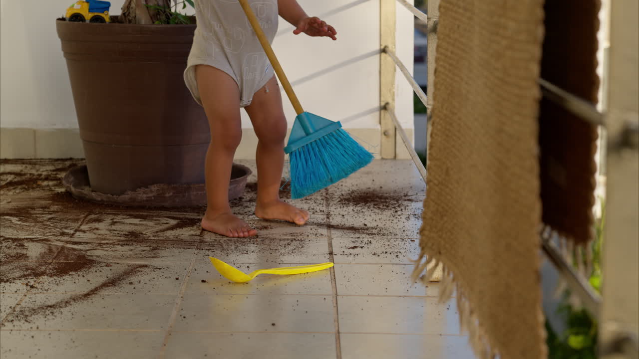 niño latino jugando con una escoba de juguete barriendo la suciedad del suelo después de hacer una travesura