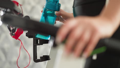 lady places bottle in holder of exercise device closeup. fit sporty woman readies rejuvenating beverage for rigorous jogging workout in apartment