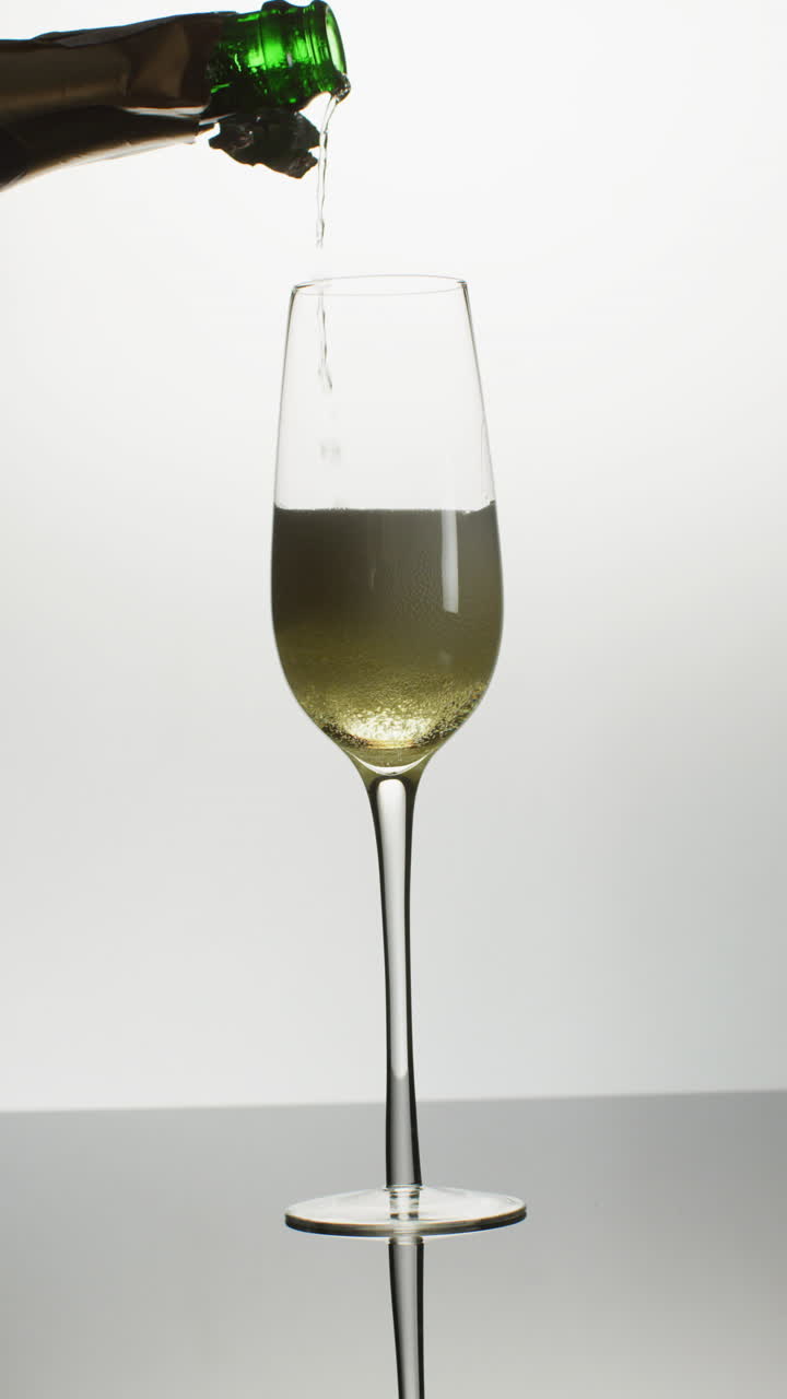 video vertical de una botella abierta vertiendo champán en un solo vaso de tulipán sobre un fondo blanco