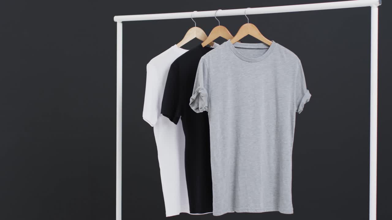 Video of three white, black and grey t shirts on hangers and copy space on black background