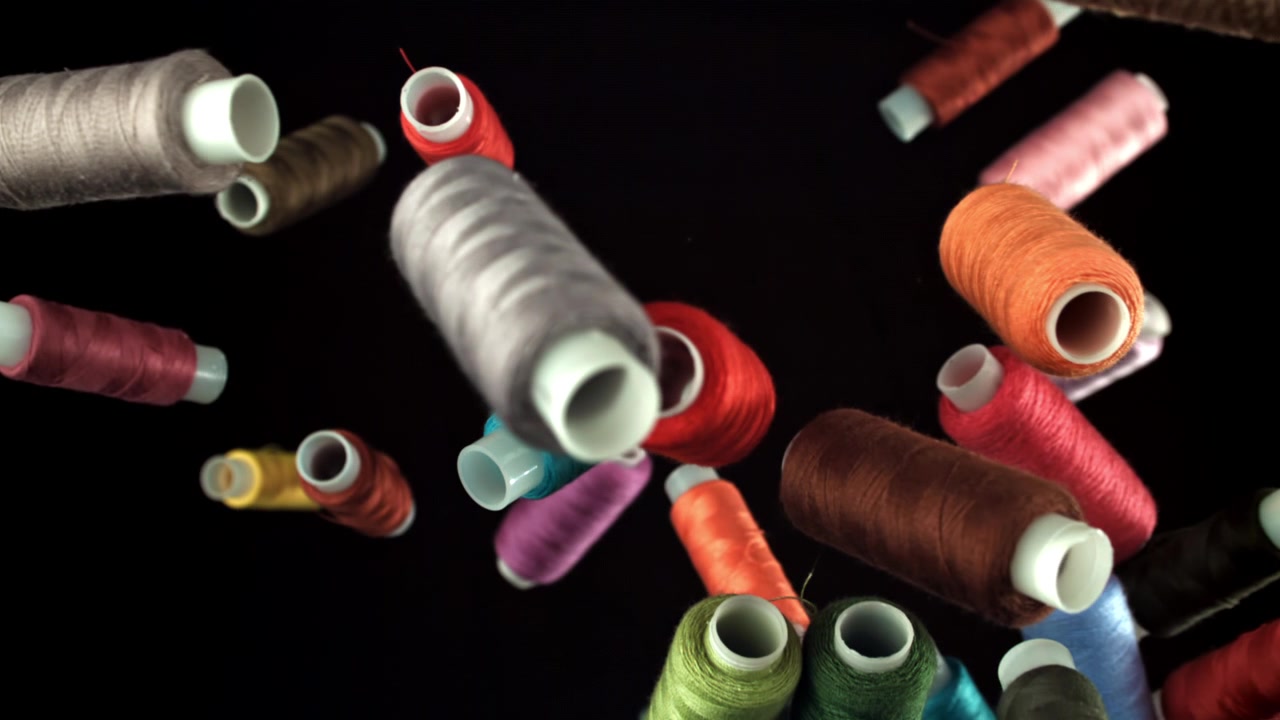 Colorful Spools of Thread Falling in Slow Motion on Black Background