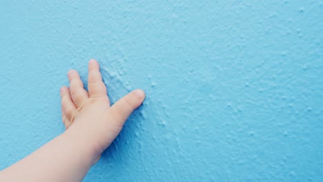 hand of a baby touches blue wall with copy space, gender reveal