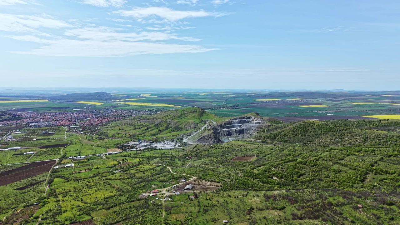 Vista de una explotación minera rodeada de exuberantes campos verdes y colinas distantes en una zona rural durante el día.