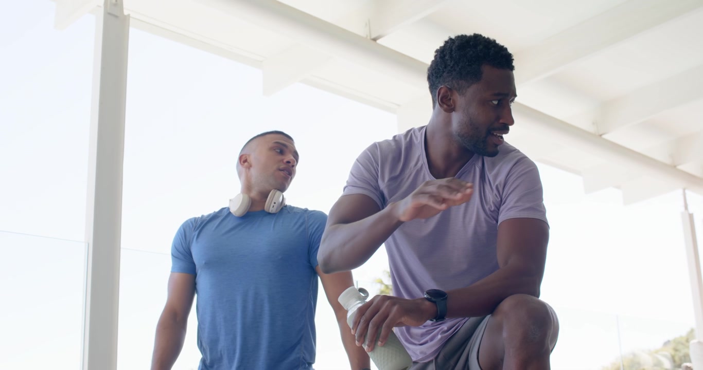 Diverse men in gym clothes taking break after set on terrace, drinking green shaker, high-fiving