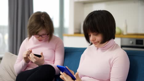 Two-girls-with-down-syndrome-are-holding-smartphones--looking-at-photos,-use-a-social-media-app