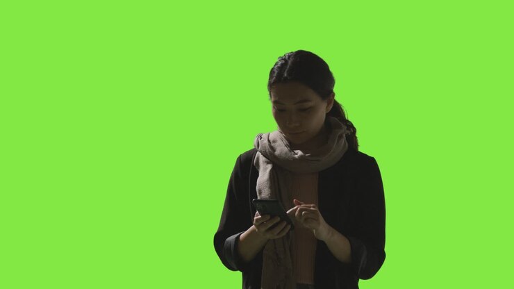 Low Key studieoptagelse af kvinde, der bruger mobiltelefon mod grøn skærm