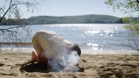 hombre soplando leña en el campamento en la playa