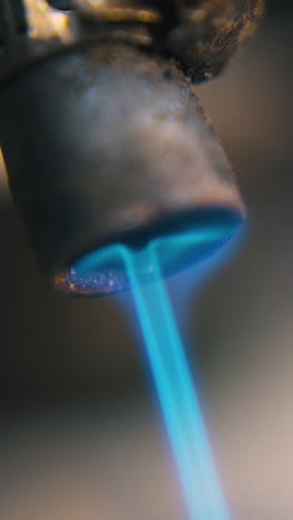 cu: old gas burner with blue color flame used to process parts of jewelry on blurred background extreme close view