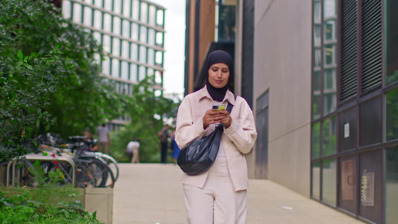 Muslim Businesswoman Wearing Hijab Going To Work Standing Outside Modern Office Looking At Mobile Phone