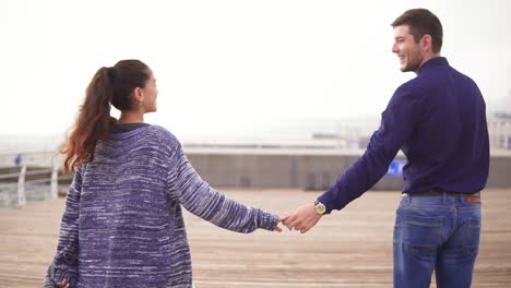 close up view of a young couple on the beach holding hands and walking together, looking in the eyes and smiling happily