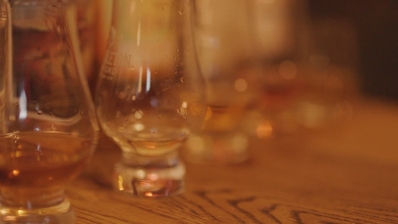 Whiskey glasses with amber liquid on rustic wood table, cozy warm lighting, shallow focus