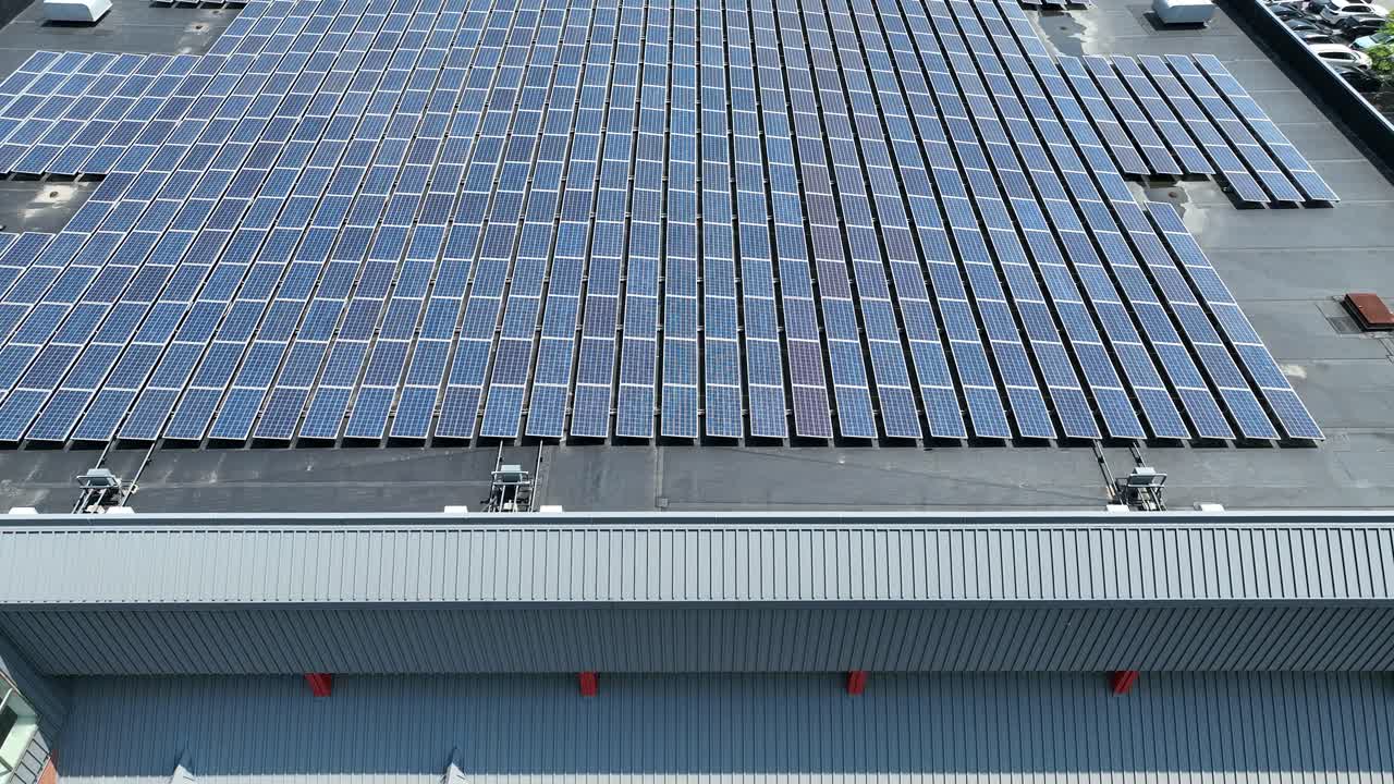 Aerial pullback across large industrial roof with organized column rows of solar panels