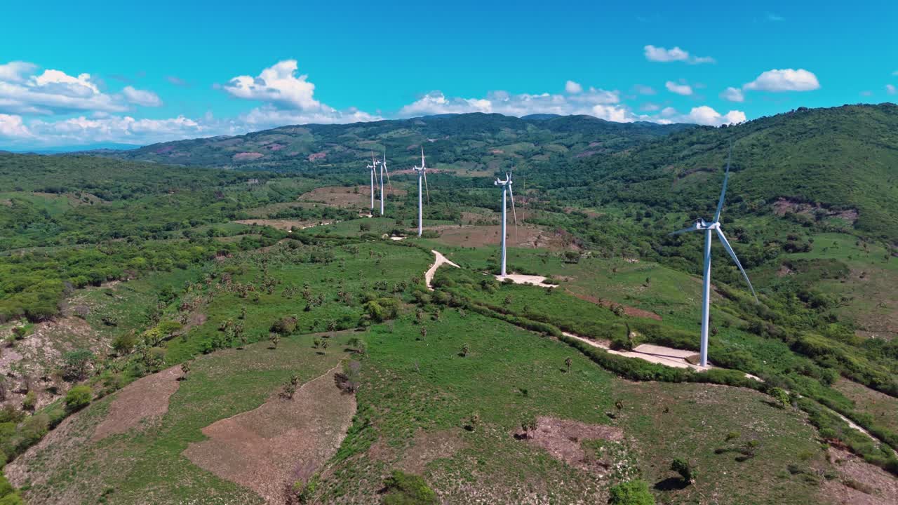Aerial drone view of wind farm on lush green hills under blue sky, producing sustainable and renewable energy, Barahona, Dominican Republic
