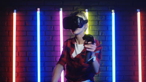 mujer joven con gafas vr y usando joystick mientras juega un juego de realidad virtual en una habitación con coloridas lámparas de neón en la pared 2