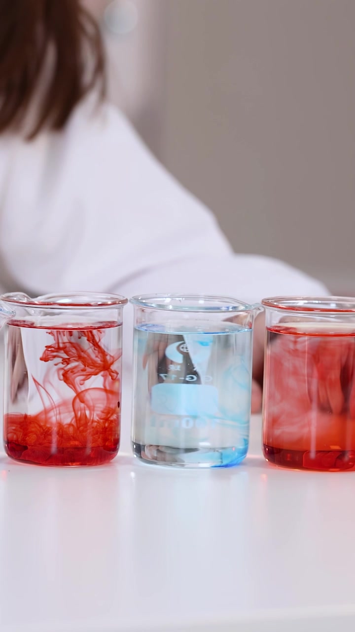 Primo piano di uno studente che mescola liquidi colorati in becher di vetro durante una lezione di scienze scolastica