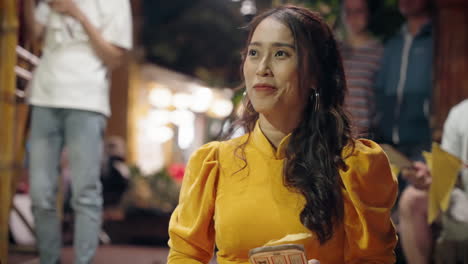 joven vietnamita con traje amarillo tradicional agita la bandera y sonríe jugando al juego bai choi en hoi an
