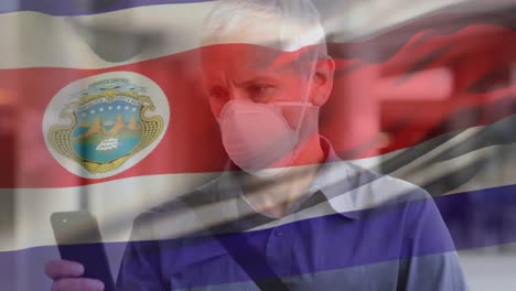 animación de agitar la bandera de costa rica sobre un hombre caucásico con máscara facial usando un teléfono inteligente en la calle