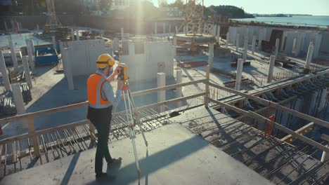 construction worker using theodolite surveying optical instrument for measuring angles in horizontal and vertical planes on construction site. worker in hard hat making projections for the building.