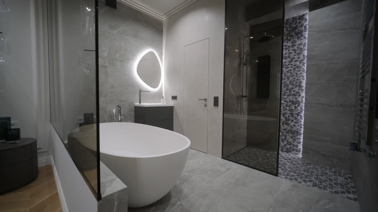 A luxurious bedroom with a stylish tufted headboard and a striking blue rug seamlessly transitions into a sleek bathroom with modern fixtures and a unique oval mirror, capturing a design that melds comfort with elegance.
