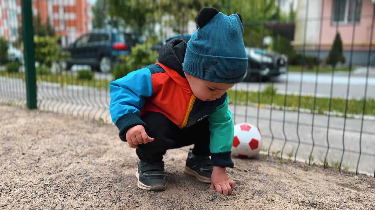 Baby boy touches the sand on the playground. Kid takes a handful of sand and throws it through the sand.