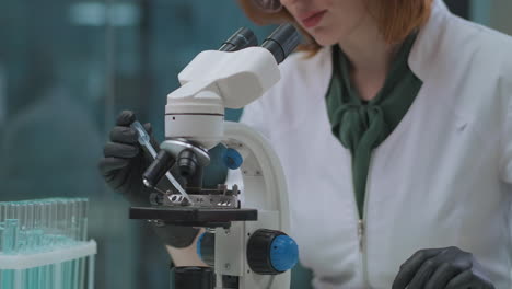 La-Química-Femenina-Está-Trabajando-Con-Reactivos-Y-Productos-Químicos-En-El-Laboratorio-Tomando-Muestras-De-Tubos-De-Ensayo-Y-Mezclando-Bajo-El-Microscopio-Investigando-La-Reacción