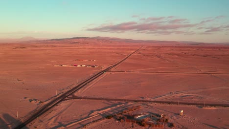 Vista-Aérea-De-Una-Calle-única-En-El-Desierto-Norte-De-Chile-Con-Las-áridas-Montañas-Al-Fondo,-Puesta-De-Sol,-Región-De-Coquimbo