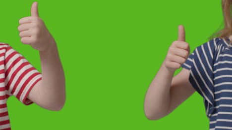 Close-Up-Of-Two-Young-Children-Giving-Thumbs-Up-Gesture-To-Camera-Against-Green-Screen