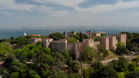 Nahaufnahme-Des-Luftwagens-Mit-Blick-Auf-Das-Alte-Traditionelle-Schloss-Auf-Der-Spitze-Des-Hügels-In-Lissabon-Mit-Der-Portugiesischen-Flagge,-Die-Im-Wind-Weht